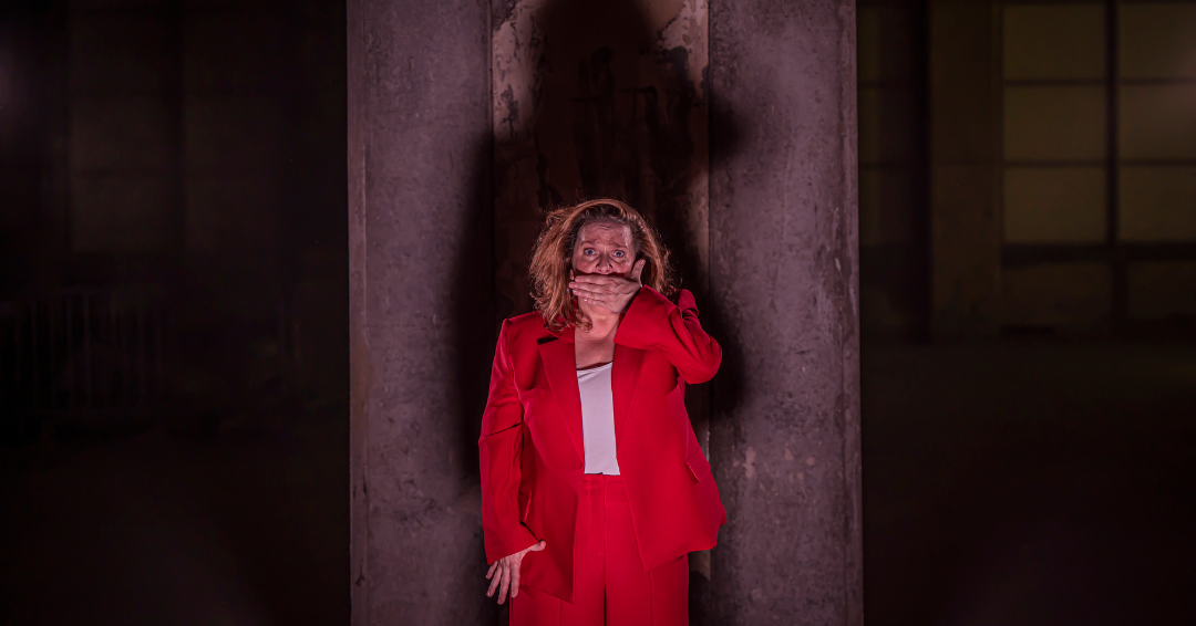 Woman wearing a red suit with her hand over her mouth.